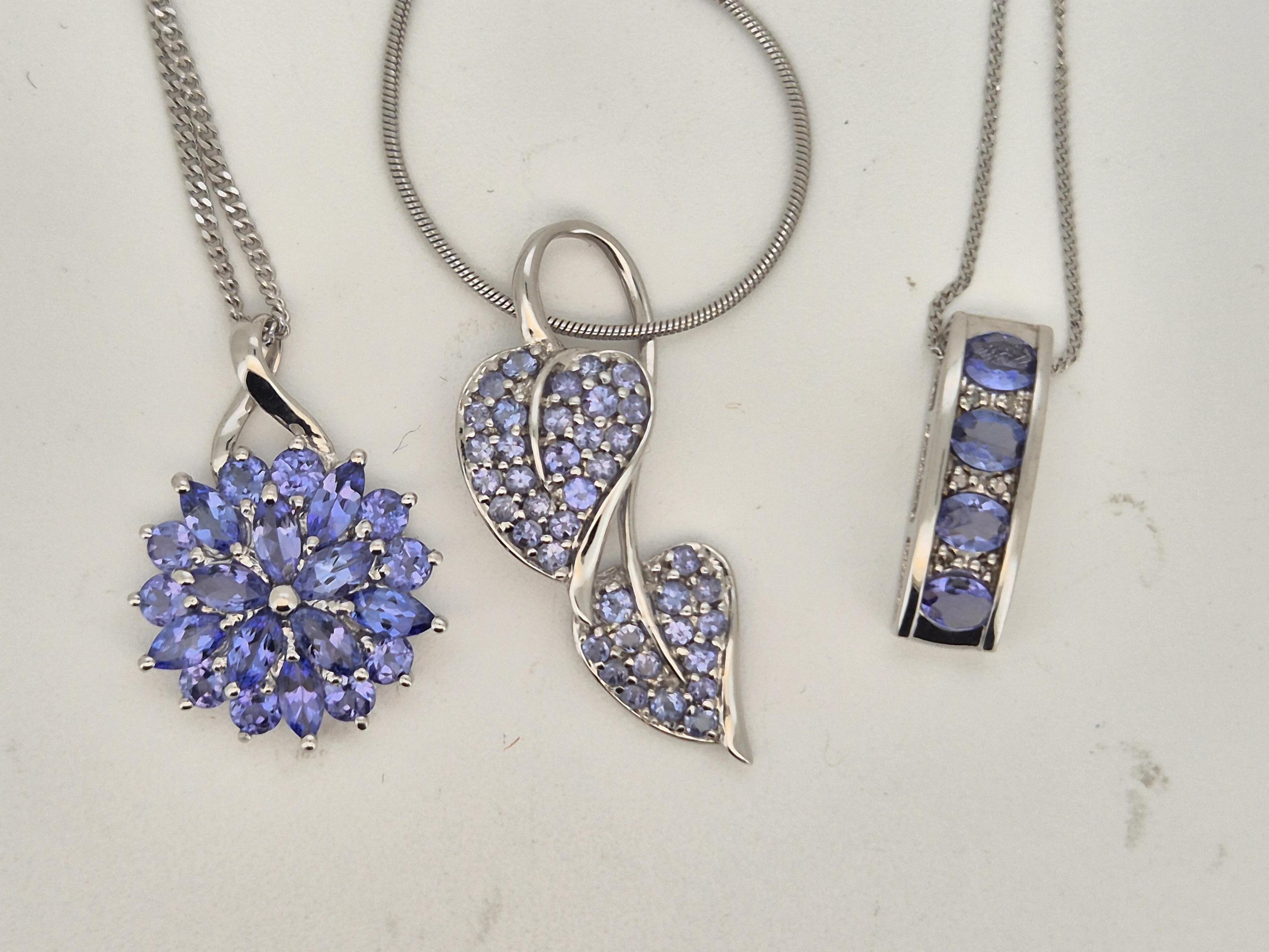 A modern 10k white metal, tanzanite and diamond chip cluster set line pendant, 17mm, on a white metal chain stamped 375, together with two other modern 9k white metal and tanzanite cluster set pendants, both on 9ct white